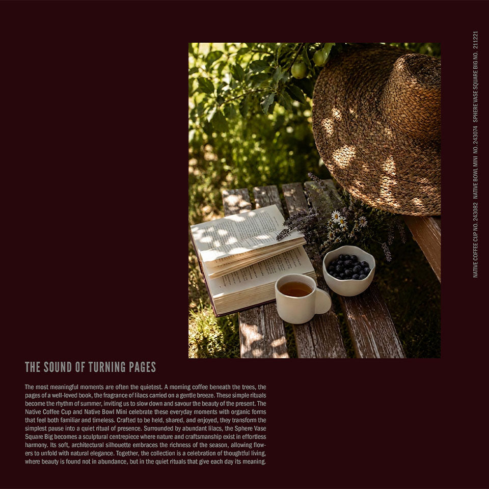A styled editorial product photo on a dark burgundy background. The central photo shows an open book on a rustic wooden table with a Native cup of tea, blueberries in a small Native bowl, and a woven straw hat in dappled sunlight.