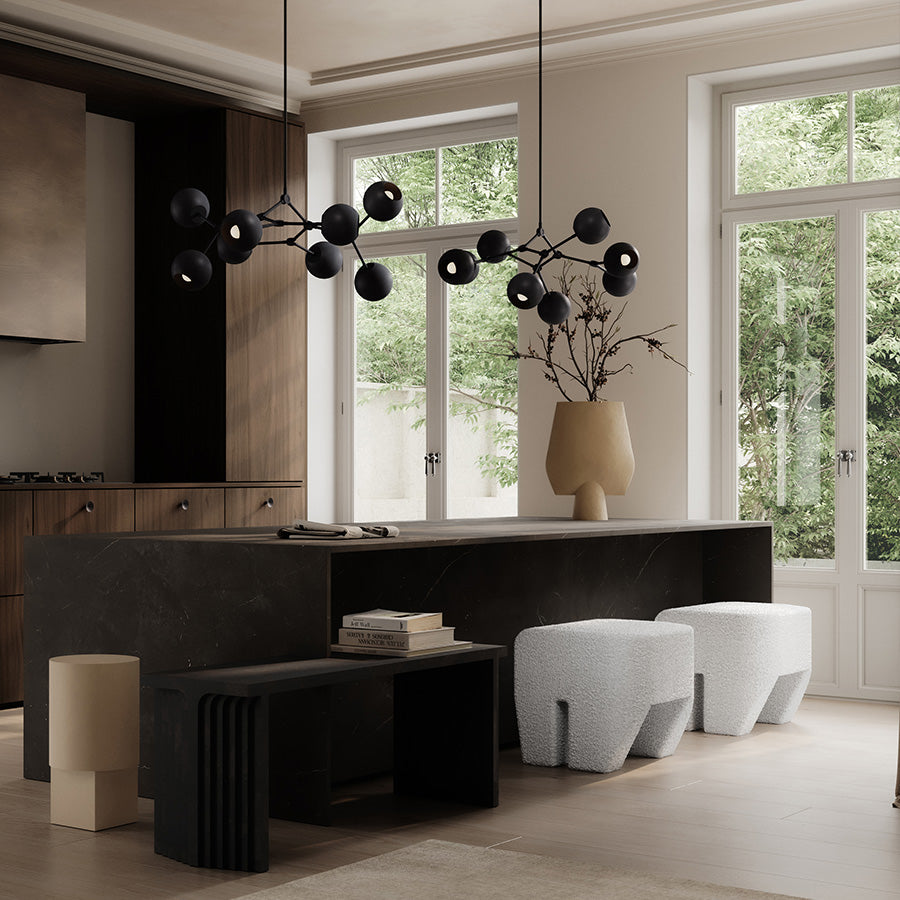 Modern kitchen with Drop Chandelier Globe and Sculpt stools, dark island, white cabinets, and large windows.