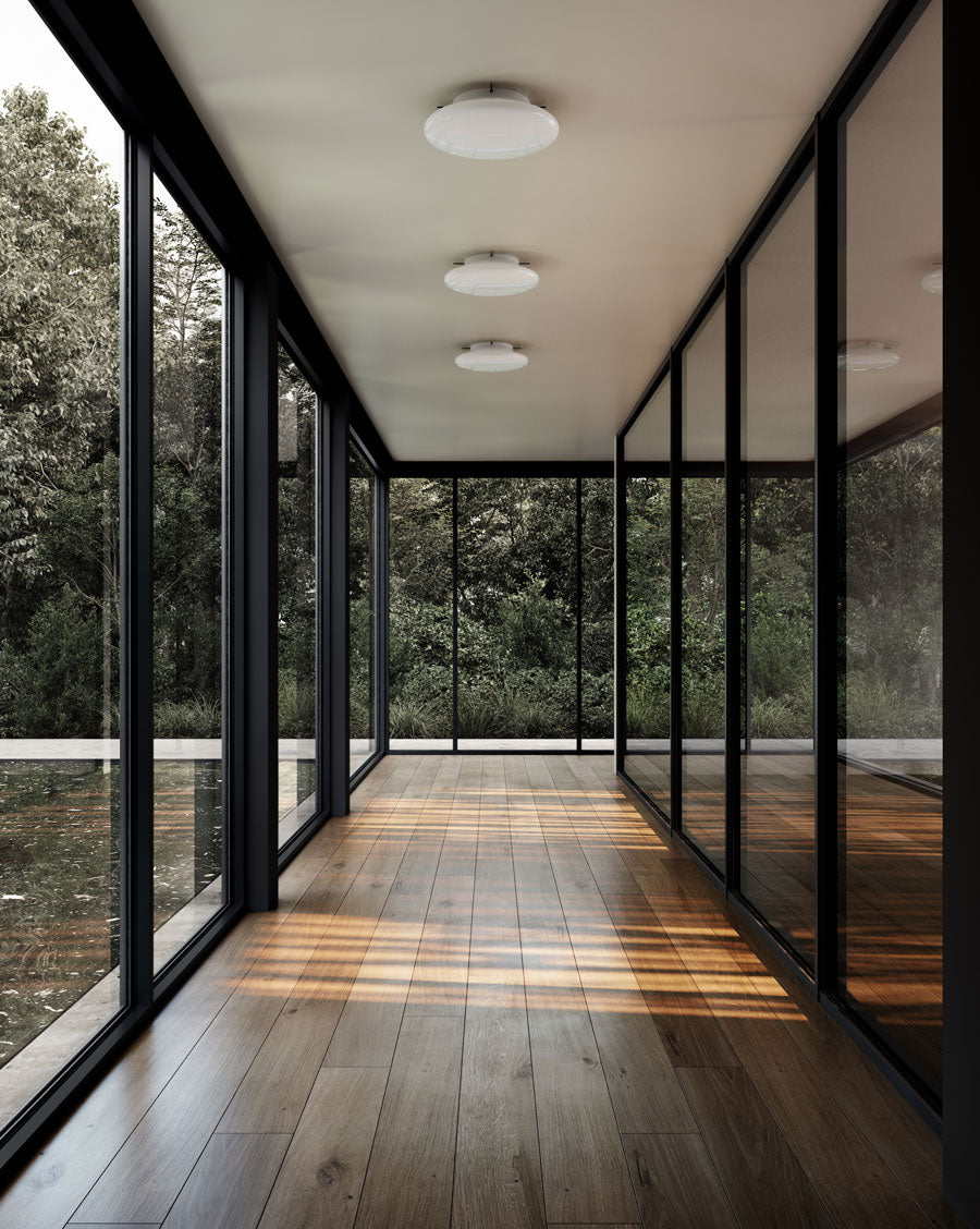 Modern interior with large glass windows and wooden floor, surrounded by greenery outside and Hikari wall lamps in Opal glass