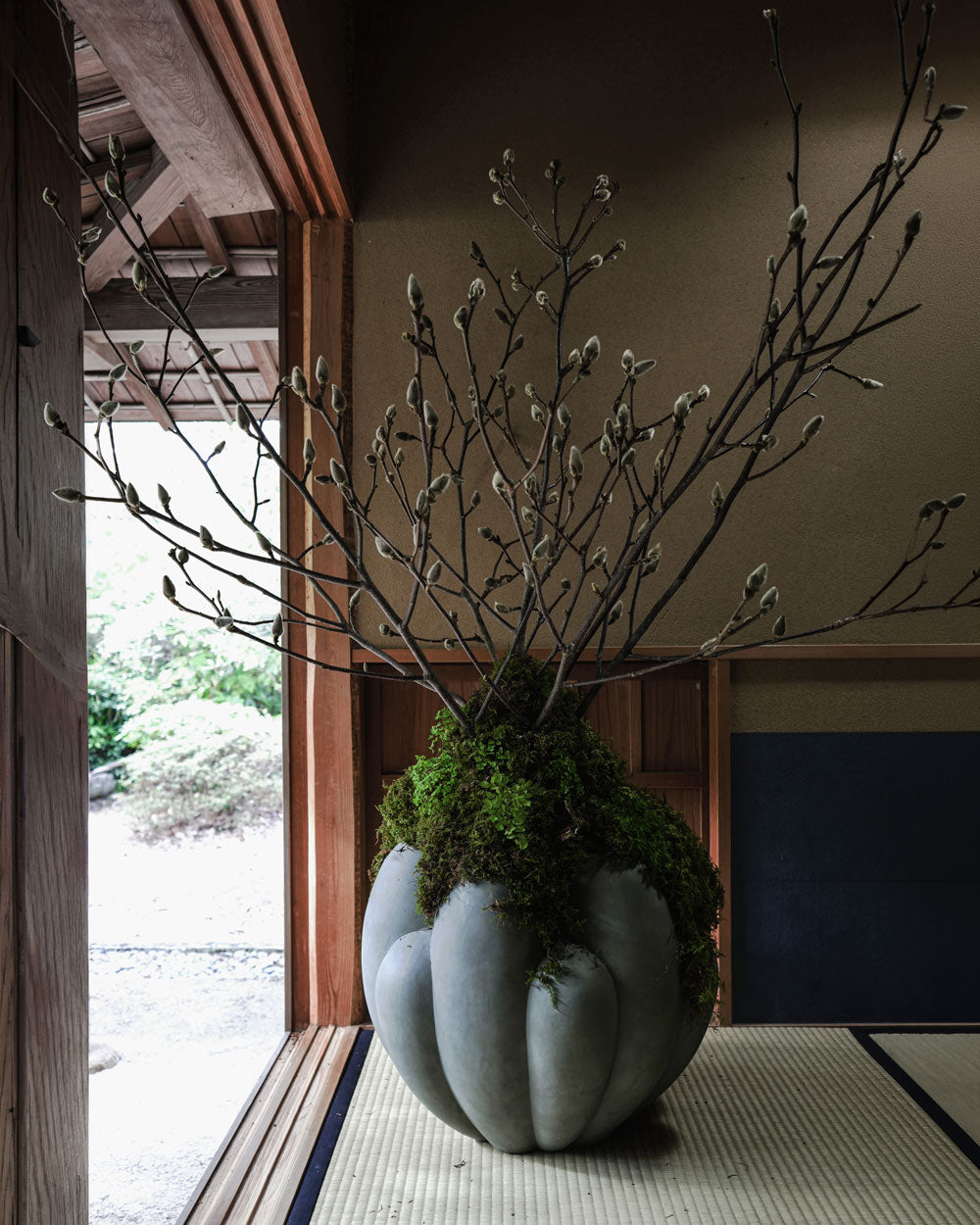 Decorative arrangement by Hikaru Seino with branches and moss in a large Bloom vase on a tatami mat floor.
