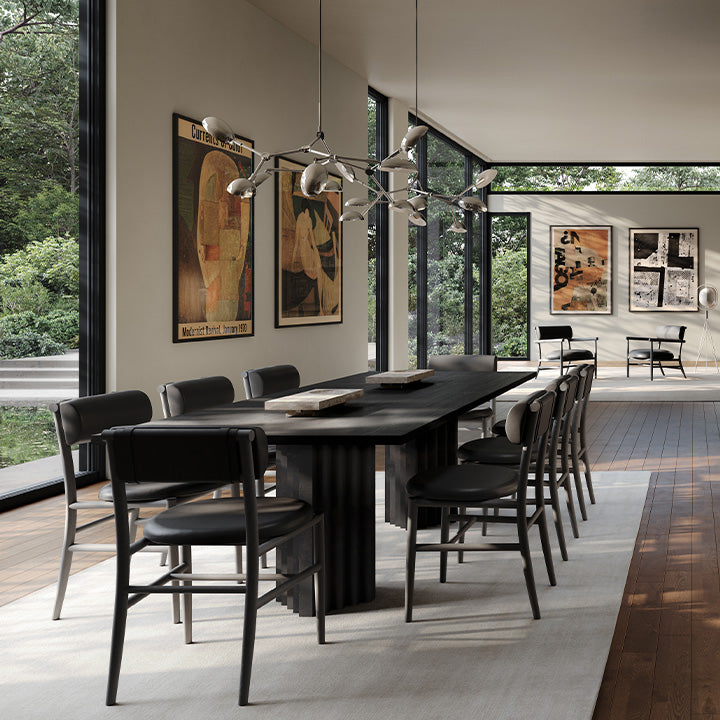 Modern dining room with a long black Arc dining table and Nama dining chairs, and Drop Chandelier in Chrome large windows, and artwork on the walls.